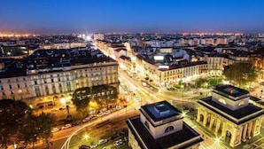 Une vue urbaine au crépuscule, avec des bâtiments illuminés et un monument historique imposant au premier plan.