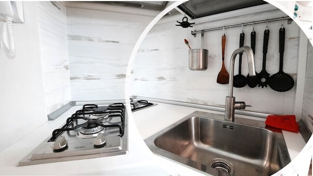 Une cuisine équipée d’une cuisinière à gaz, d’un évier en acier inoxydable et d’ustensiles suspendus.