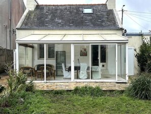 A single-story house with a glass conservatory. Inside, there is a dining table with chairs and a white chair. - Maison Proche de Brest Arena (Brest)