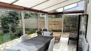 A conservatory with a dining table and chairs, a small seating area, and a view of the garden. - Maison Proche de Brest Arena (Brest)