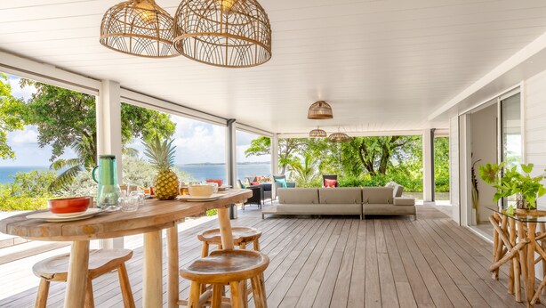 Una terraza de madera con una mesa, taburetes, un sofá y vista al océano.