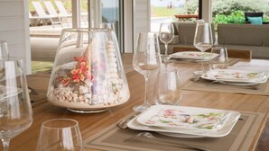 Una mesa de comedor decorada con cristalería transparente, platos con motivos florales y un cuenco de vidrio decorativo con guijarros y flores.