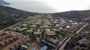 Vista aérea de uma área residencial costeira com várias casas, piscinas e uma estrada que leva ao mar.