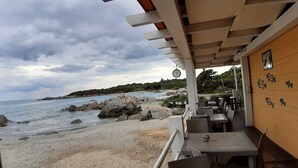 Um restaurante à beira-mar com área externa, vista para o mar e parede de madeira com detalhes decorativos.
