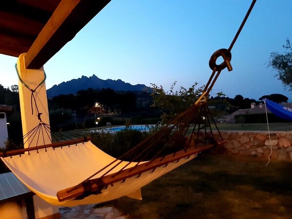A hammock suspended by ropes, a stone wall, and a pool in the background.