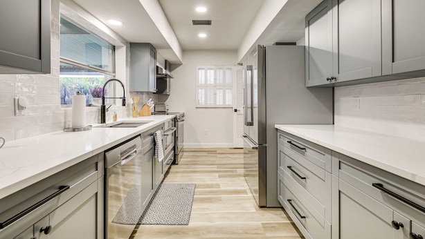 Una cocina moderna con armarios blancos, electrodomésticos de acero inoxidable y piso de madera clara.