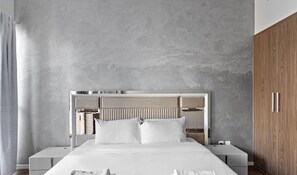 A modern bedroom with a large bed, a headboard with built-in lighting, bedside tables, and a wooden wardrobe.