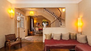 Un vaste salon doté d’un plancher en bois, d’un canapé rouge, d’une chaise en bois, d’un escalier et d’un coin repas à l’arrière-plan.