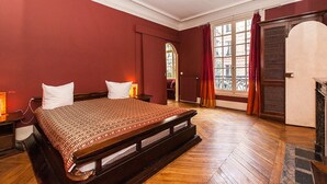 Une chambre traditionnelle avec un grand lit, un plancher en bois et une fenêtre avec des rideaux.