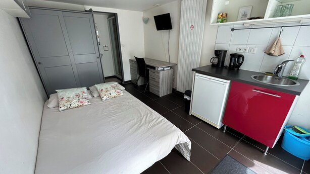 A compact room with a bed, a small desk, a kitchenette, and a TV mounted on the wall. - Studio Pour Votre Séjour à Paris (Châtillon)