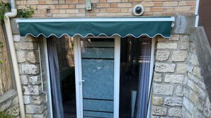 A small, stone-walled building with a green awning over a sliding glass door. - Studio Pour Votre Séjour à Paris (Châtillon)