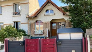 A two-story house with a garage door, a balcony, and a small porch. - Studio Pour Votre Séjour à Paris (Châtillon)
