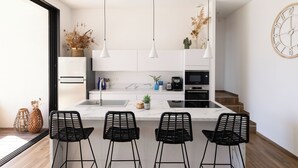 Una cocina moderna con una isla central, taburetes de bar, luces colgantes y un reloj en la pared.