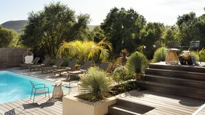 Un área junto a la piscina con sillones de descanso, una pequeña mesa y escalones que llevan a una terraza.