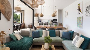 Una sala moderna con sofá seccional, comedor y cocina al fondo.