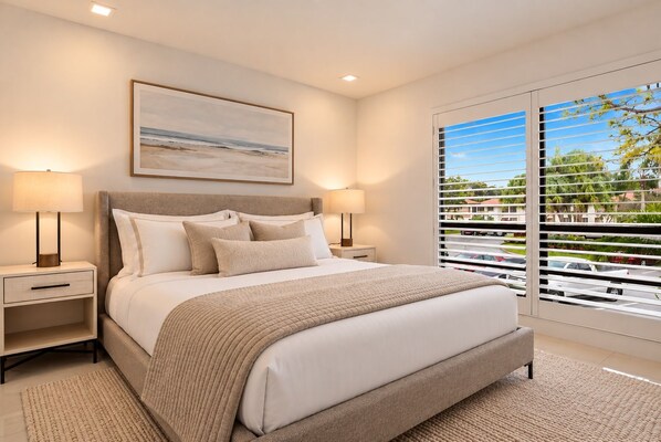 Une chambre à coucher moderne avec un grand lit, deux tables de chevet, une commode, une fenêtre avec des stores et un tableau au mur.