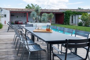 A long dining table with chairs, a pool, and a building with a red exterior in the background. - Hécate - Superb family home in Loix (LOIX)