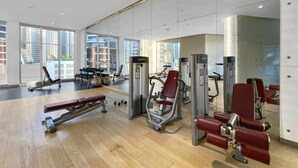A gym with various exercise equipment, large windows, and a wooden floor.