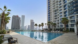 A swimming pool with lounge chairs and palm trees, surrounded by high-rise buildings.