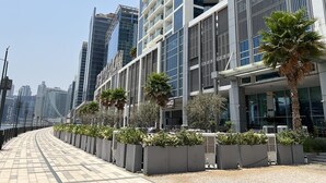 A modern urban building with a glass facade, a pedestrian walkway, and palm trees.