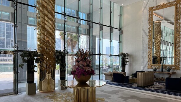 A modern lobby with large windows, a central decorative column, and a large mirror.