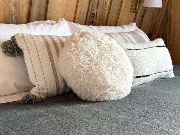 Una cama con un colchón gris, almohadas blancas y un almohador mullido.