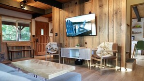 Una sala de estar acogedora con paredes de madera, un televisor montado en la pared y una zona de estar cómoda con un sofá y sillones.