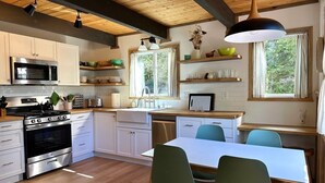 Una cocina moderna con piso de madera, gabinetes blancos, una estufa de acero inoxidable y un comedor con mesa y sillas.