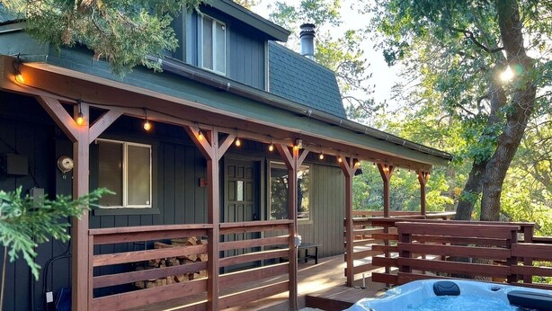 Un espacio al aire libre techado con un jacuzzi, bancos de madera y luces colgantes.