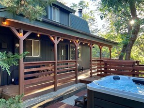 Un espacio al aire libre techado con un jacuzzi, bancos de madera y luces colgantes.