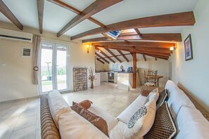 A spacious living area with a high ceiling and exposed wooden beams, a built-in kitchen, and a sliding glass door leading to an outdoor area. - Mearbeck House, Penthouse. Agios Nikolaos, Notos, Petreti, Boukari  (Petreti  Corfu)