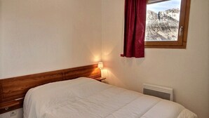 A single bed with a wooden headboard, a bedside lamp, a window with a red curtain, and a radiator.