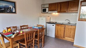 A compact kitchen with wooden cabinets, a microwave, a dishwasher, and a dining table with chairs.