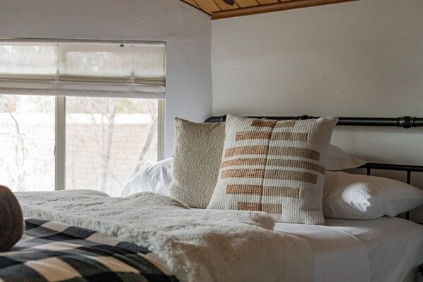 Un lit avec un oreiller à rayures et un oreiller uni, une fenêtre avec des stores et un plafond en bois.