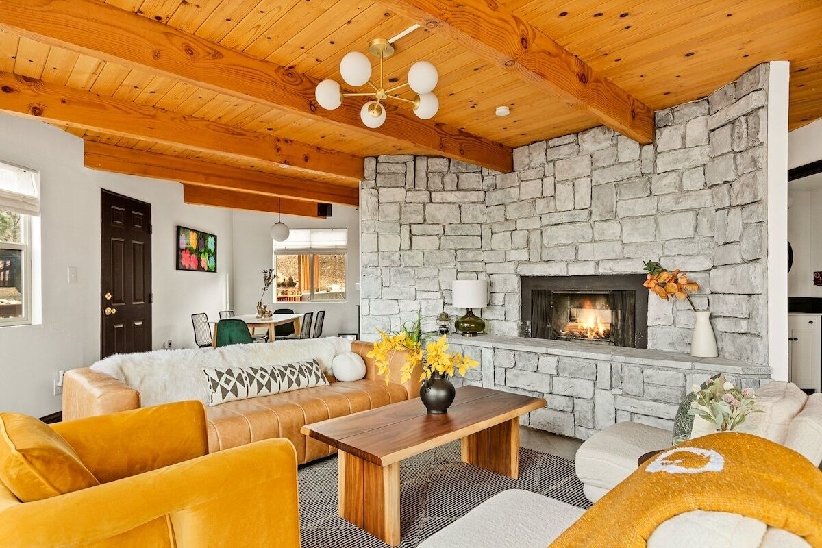 A living room with a stone fireplace, wooden ceiling beams, and a sofa set.