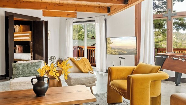 A cozy living room with a sofa, ottoman, and a foosball table. - Heart of Big Bear | Lake & Mountain View (Big Bear Lake)
