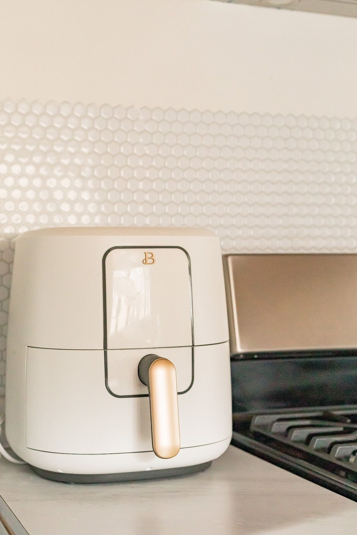 Une friteuse à air blanche, dotée d’un panneau de commande et d’une poignée dorée, posée sur un plan de travail de cuisine.