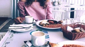 Eine Person sitzt an einem Tisch mit einer Portion Bohnen und einer Kaffeetasse.