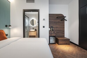 A modern hotel room with a large bed, a bathroom with a mirror, and a wooden accent wall.