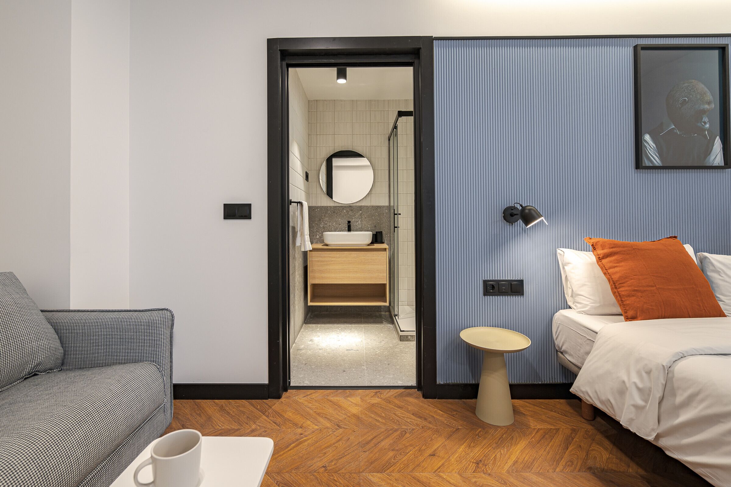 A modern hotel room with a sofa, a bed, a small table, and a bathroom visible through an open door.