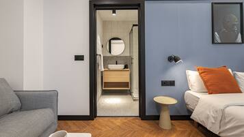A modern hotel room with a sofa, a bed, a small table, and a bathroom visible through an open door.