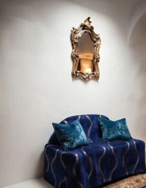 A room with a blue sofa and two pillows, a wall-mounted mirror, and a light fixture. - Hidden Garden Boutique Apartment in Campo de' Fiori (Roma)