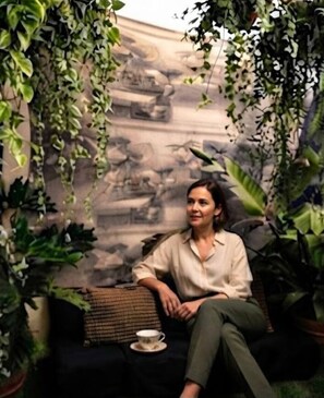 A person sitting on a couch with a cup on a saucer, surrounded by greenery and a stone wall. - Hidden Garden Boutique Apartment in Campo de' Fiori (Roma)