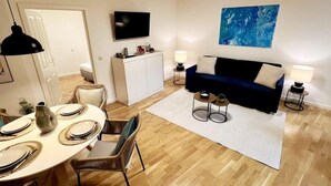 A modern living room with a dining area, a sofa, a flat-screen TV, and a blue abstract painting. - Beckhomes: Luxus-apartment Direkt in der Altstadt (Bamberg)