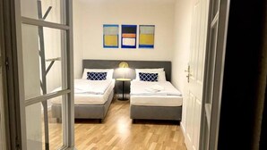 A hotel room with two beds, a bedside table, and a lamp. There are three abstract paintings on the wall. - Beckhomes: Luxus-apartment Direkt in der Altstadt (Bamberg)