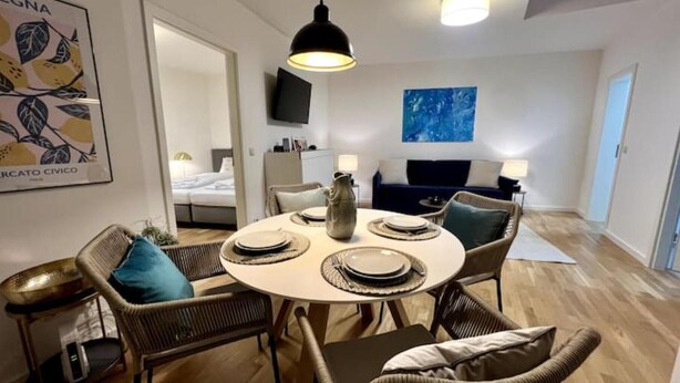 A dining area with wicker chairs, a round table, and a vase. There is a bed and a TV in the background. - Beckhomes: Luxus-apartment Direkt in der Altstadt (Bamberg)