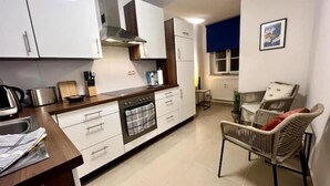 A compact kitchen with white cabinets, a stove, and a dining area with wicker chairs. - Beckhomes: Luxus-apartment Direkt in der Altstadt (Bamberg)