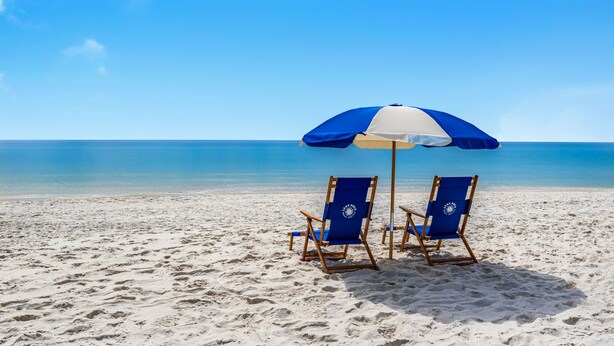 Une plage avec deux chaises de plage bleues sous un parasol bleu et blanc.