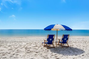Une plage avec deux chaises de plage bleues sous un parasol bleu et blanc.