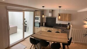 A modern kitchen with wooden cabinets, a dining table with four chairs, and a sliding glass door leading to a balcony. - Maison Pêcheur Cosy Proche Plage et Port 6pers (Les Sables-d'Olonne)